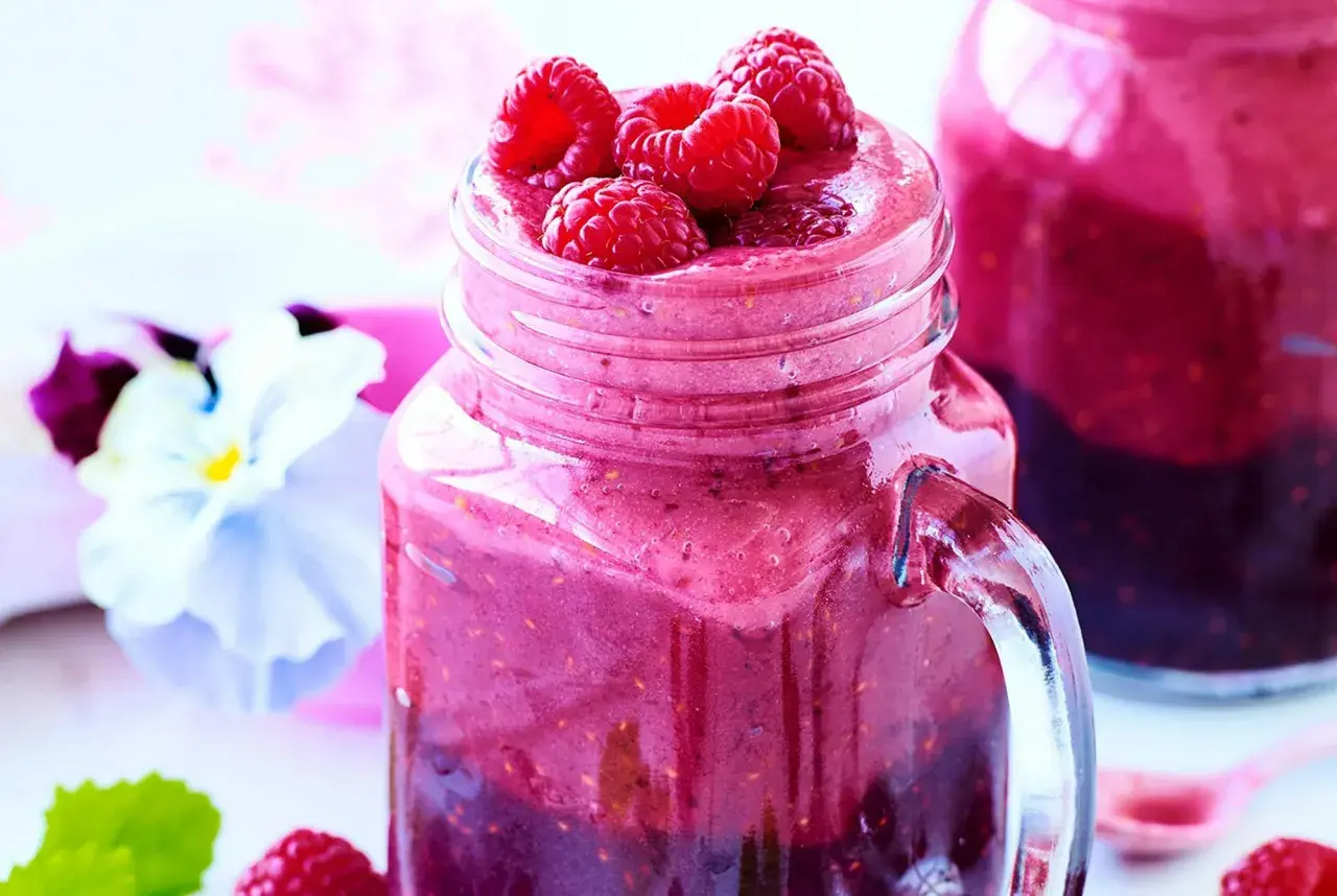 En härlig hallonsmoothie i ett glas med färska hallon på toppen. Ett perfekt smoothie recept för en solig dag.