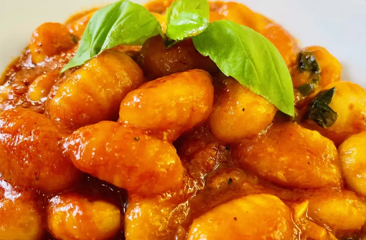 Gnocchi al pomodoro, soffici e avvolti in un sugo rosso brillante, guarniti con foglie di basilico fresco.
