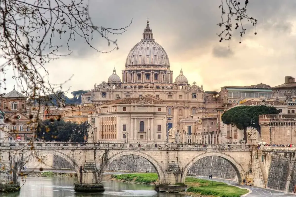 Un ponte di Roma attraversa il Tevere, con la maestosa cupola di San Pietro che domina lo skyline in una giornata invernale.
