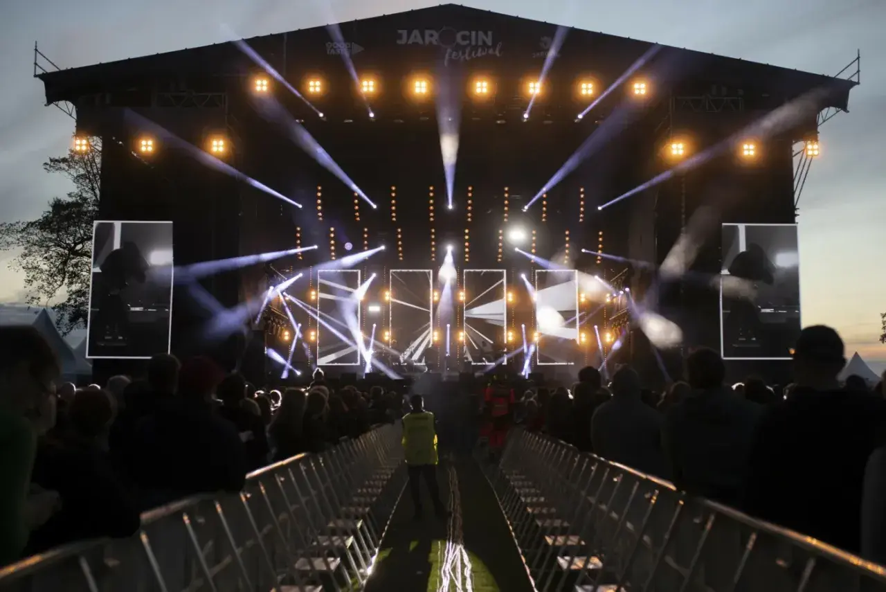 Jarocin Festival rozświetlony tysiącami świateł. Tłum czeka na koncert, a na scenie widać artystów.