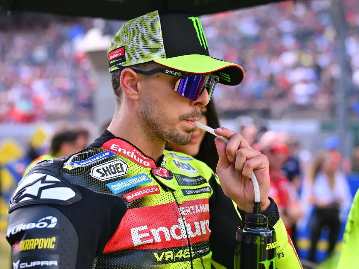 Fabio Di Giannantonio, piloto de MotoGP, bebe de una botella con un tubo, luciendo su casco y gafas de sol.