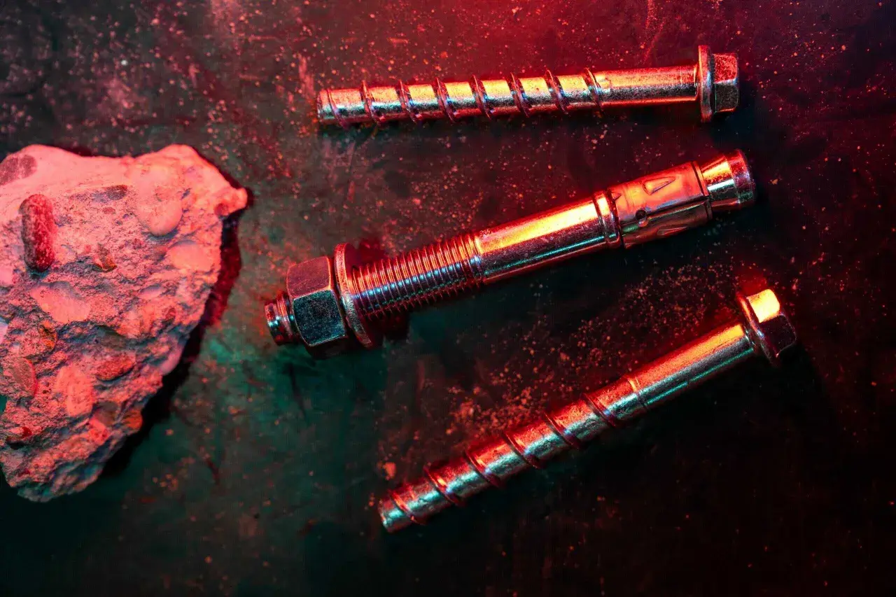 Tasselli e bulloni metallici, con un pezzo di cemento grezzo. La scena è illuminata da luci rosse e verdi, creando un'atmosfera drammatica, ideale per una tabella portata tasselli.