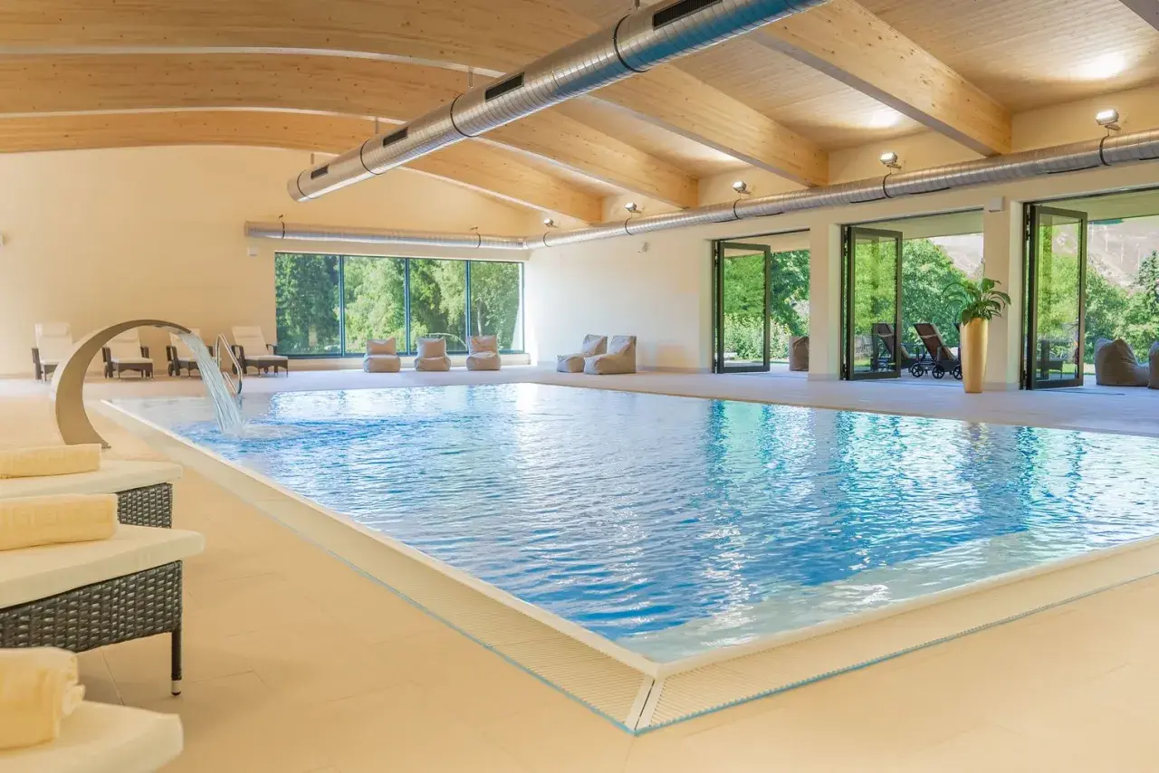 Entspannter Urlaub in Sachsen: Einladender Innenpool mit Wasserfall, Liegen und Blick ins Grüne. Perfekt für erholsame Tage.
