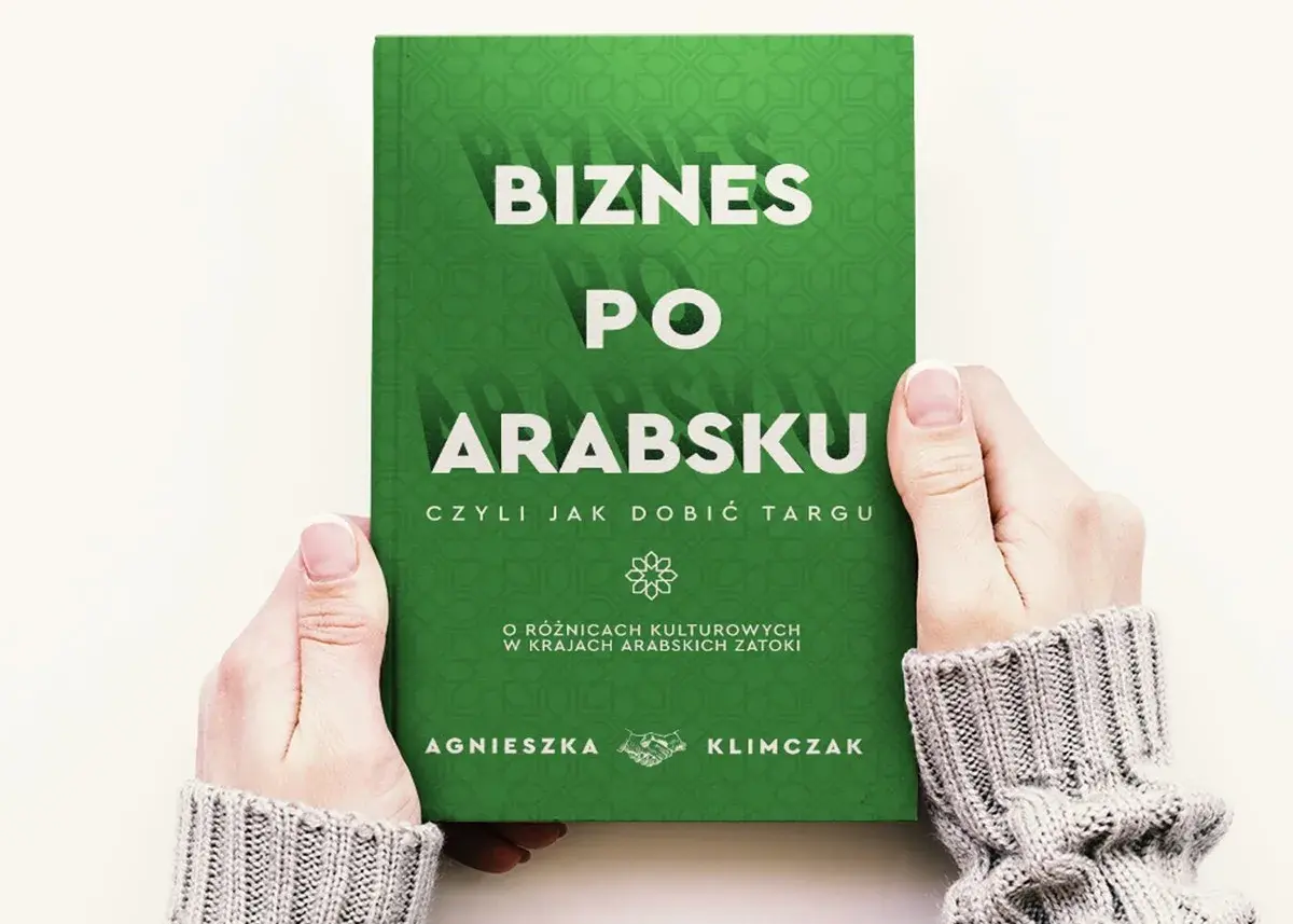 Dwie dłonie trzymają zieloną książkę z białym napisem "Biznes po arabsku".
