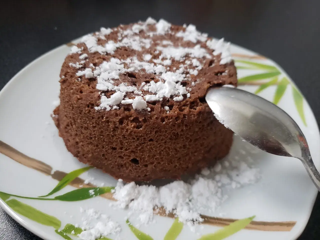Un délicieux bowl cake au chocolat, saupoudré de sucre glace, prêt à être dégusté avec une cuillère.