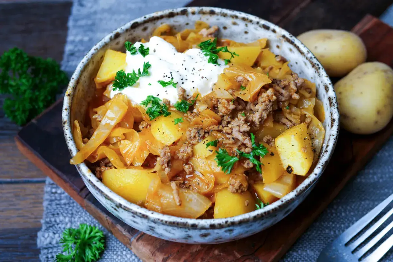 Herzhaftes Schichtkraut Rezept mit Hackfleisch, Kartoffeln und einem Klecks Sauerrahm, garniert mit Petersilie.