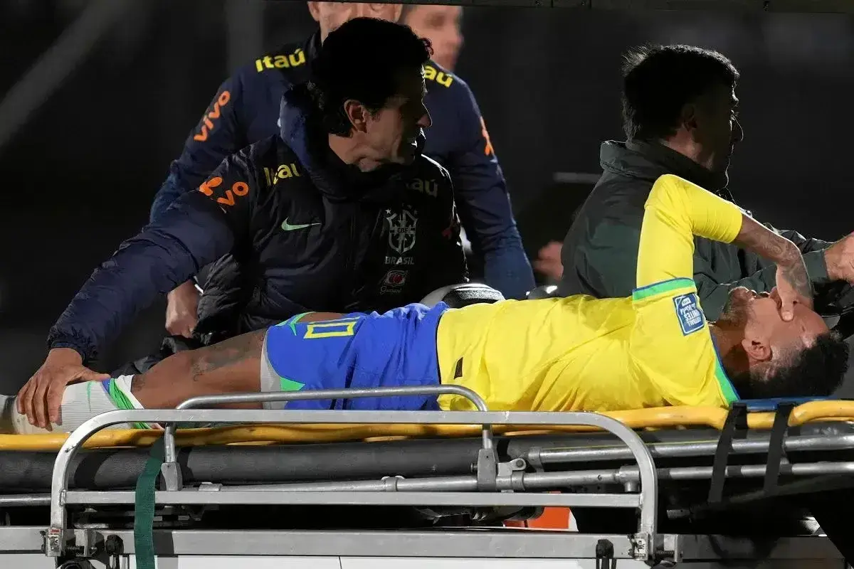 Neymar leży na noszach, z bólu trzymając się za twarz. Jego **neymar kontuzja** wygląda poważnie, a sztab medyczny otacza go troską.
