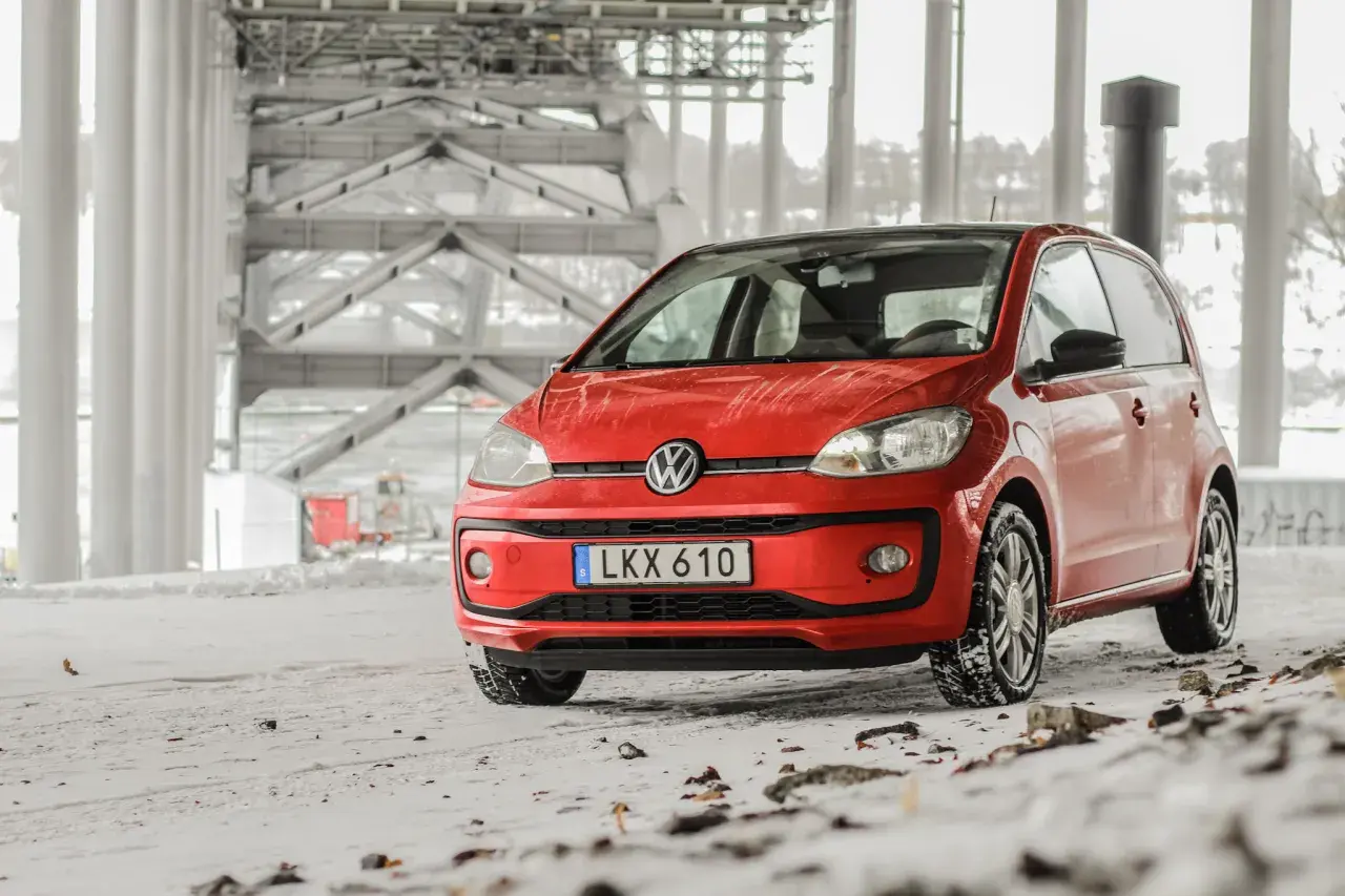 Röd VW Up med vinterdäck står på snöig mark under en bro. Ett vw up problem kan vara att den fastnar i snön.