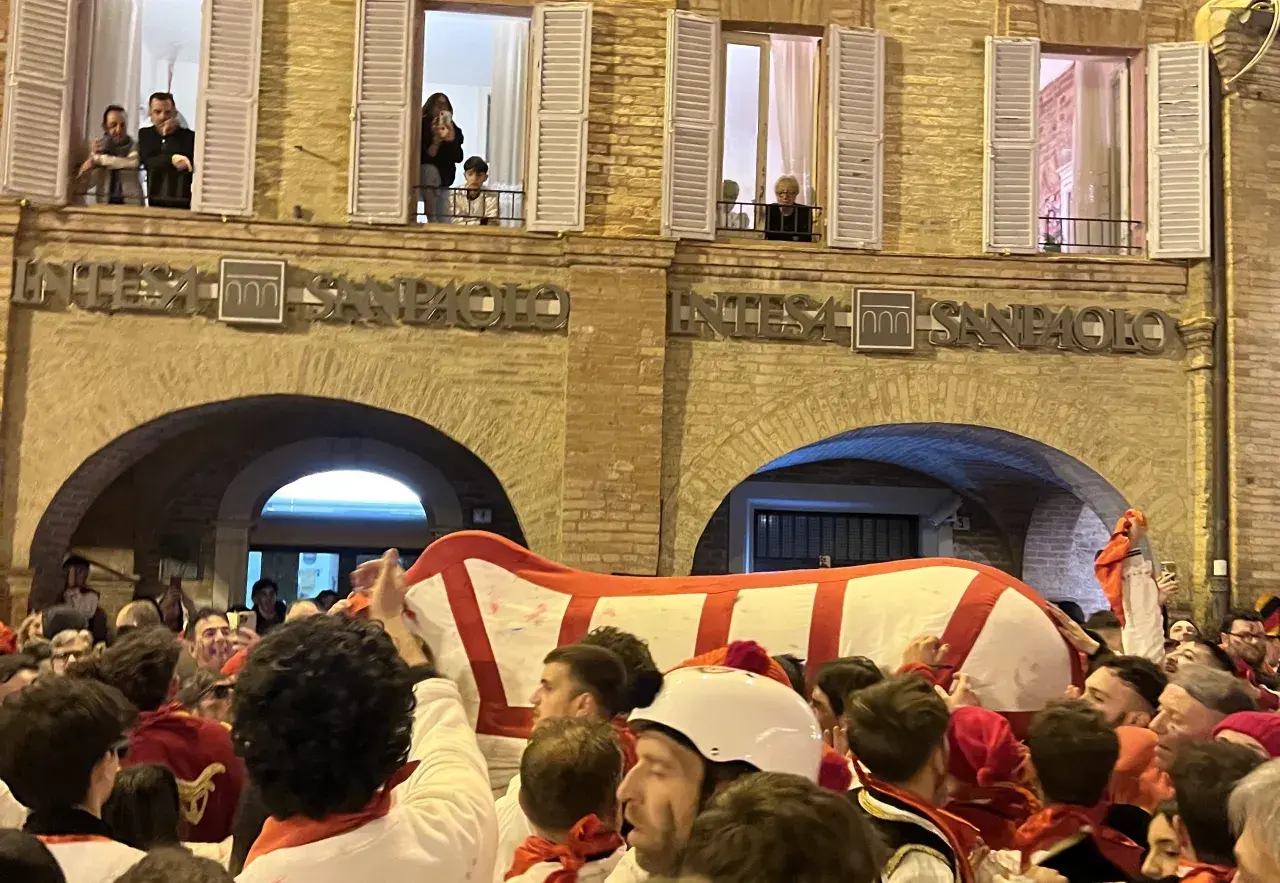 Folla festante al carnevale di Offida, con un grande carro bianco e rosso che avanza tra la gente.