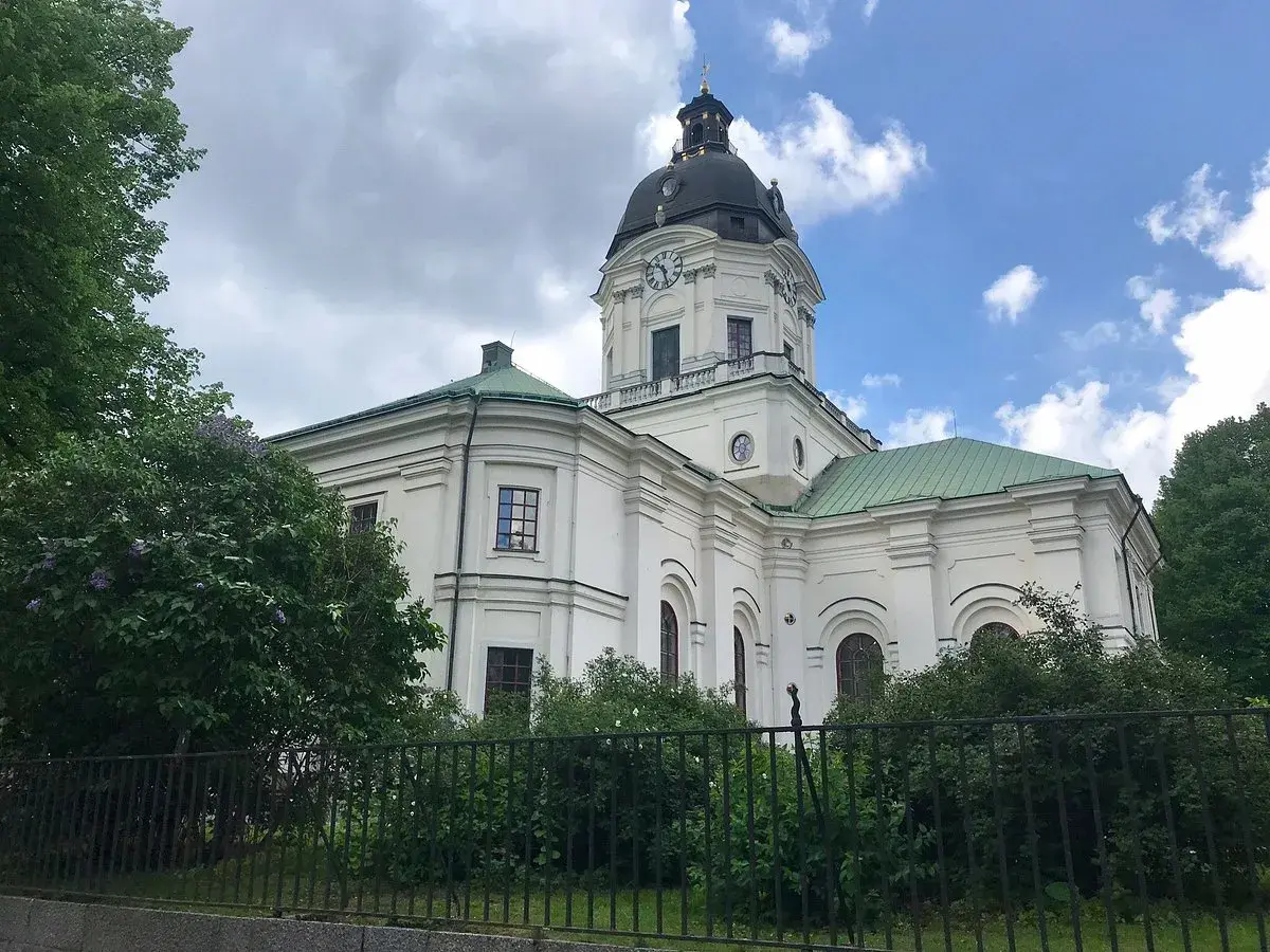 Adolf Fredriks kyrka i Stockholm, en vit kyrka med grön kupol och tak, omgiven av träd och buskar.