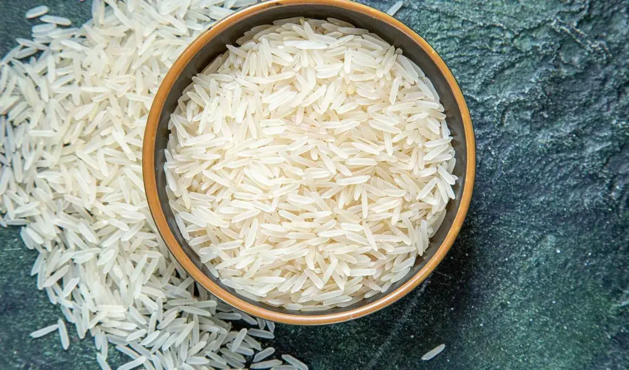 Chicchi di riso basmati in una ciotola e sparsi su una superficie scura. Le proprietà del riso basmati lo rendono un alimento leggero e digeribile.