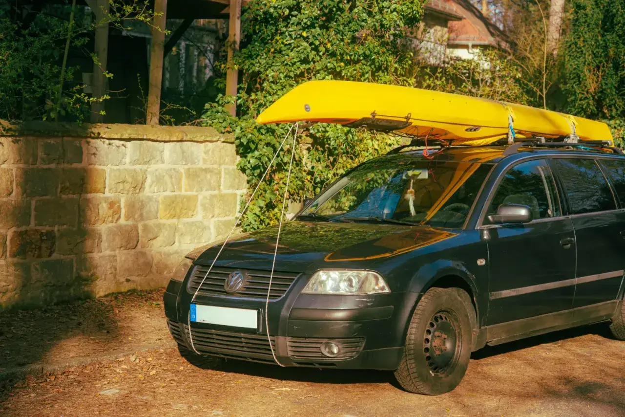 Żółty kajak na dachu czarnego kombi. Pokazuje, co można przewozić na dachu samochodu, np. sprzęt wodny.