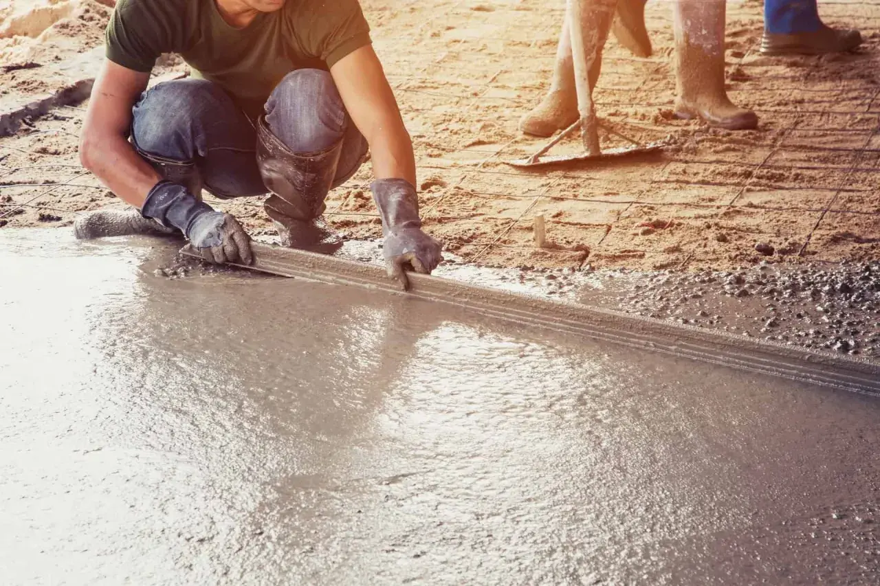 Pracownik wylewa betonową posadzkę w garażu za pomocą łaty.