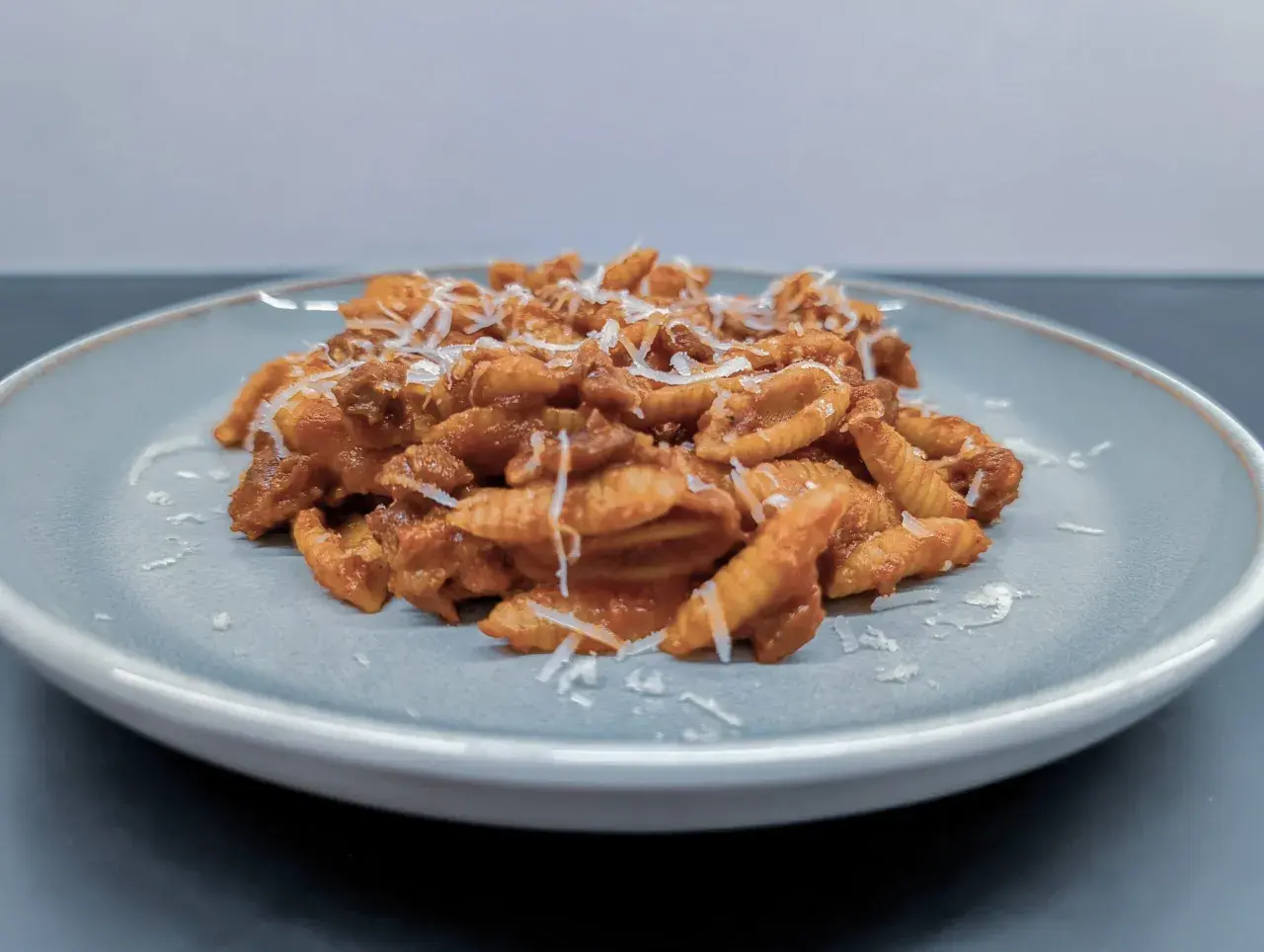Gnocchi Sardi (Malloreddus) mit Tomatensoße und geriebenem Parmesan auf einem Teller.