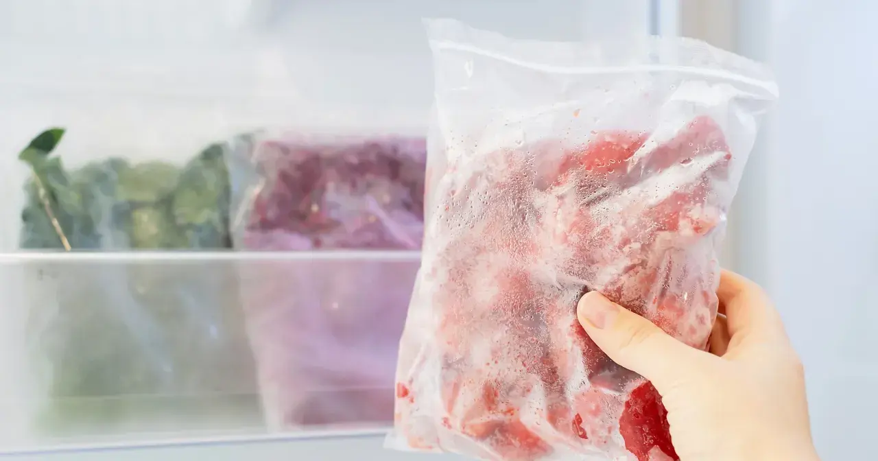 Ręka wyjmuje z zamrażarki worek z mrożonymi owocami. Czy jogurt można mrozić? Tak, ale najlepiej w małych porcjach.