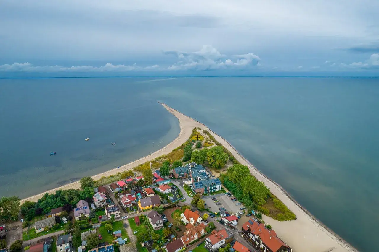 Malownicza miejscowość nad morzem z zabudowaniami i piaszczystą plażą, otoczona spokojnymi wodami.
