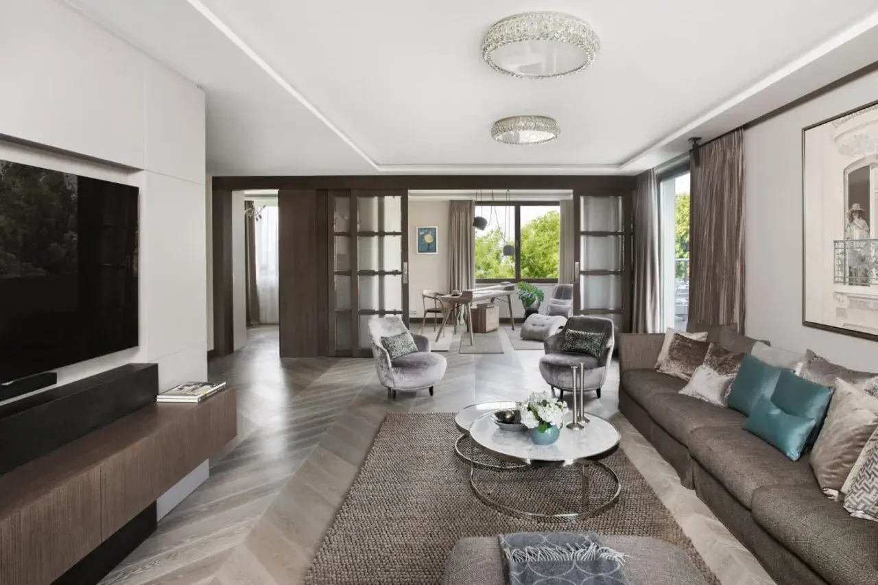 Elegancki salon w stylu klasycznym wnętrza, z wygodną kanapą, okrągłymi stolikami i przeszklonymi drzwiami prowadzącymi do jadalni.