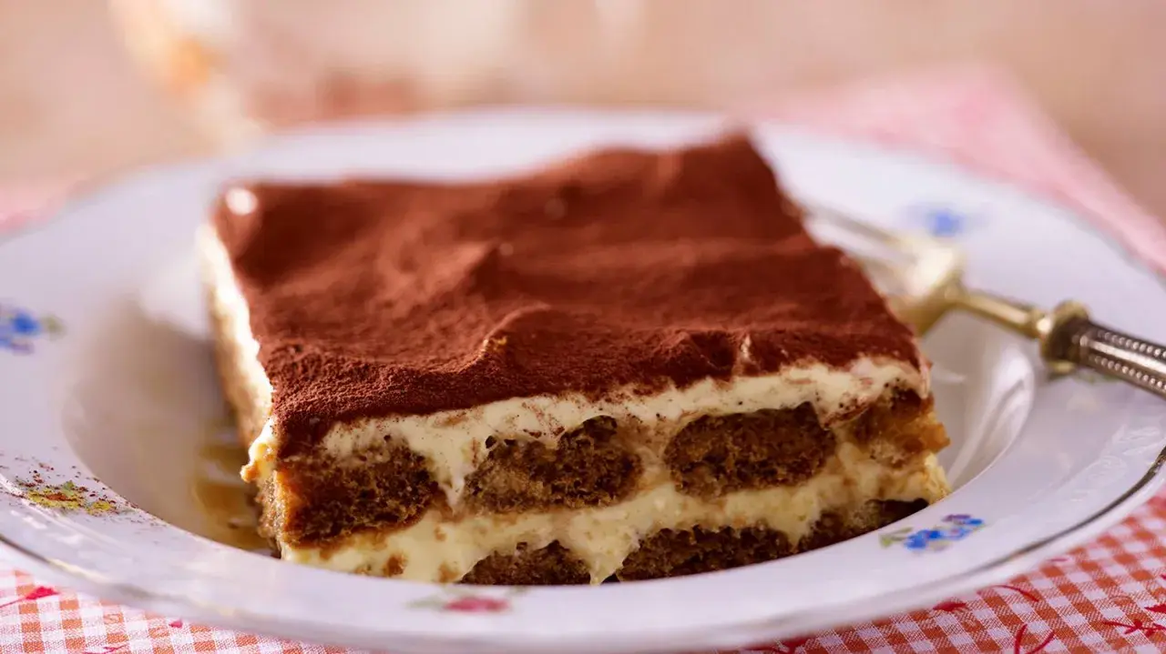 Ein Stück Tiramisu, ein Klassiker der italienischen Nachspeisen, auf einem Teller mit Kakaopulver bestäubt.