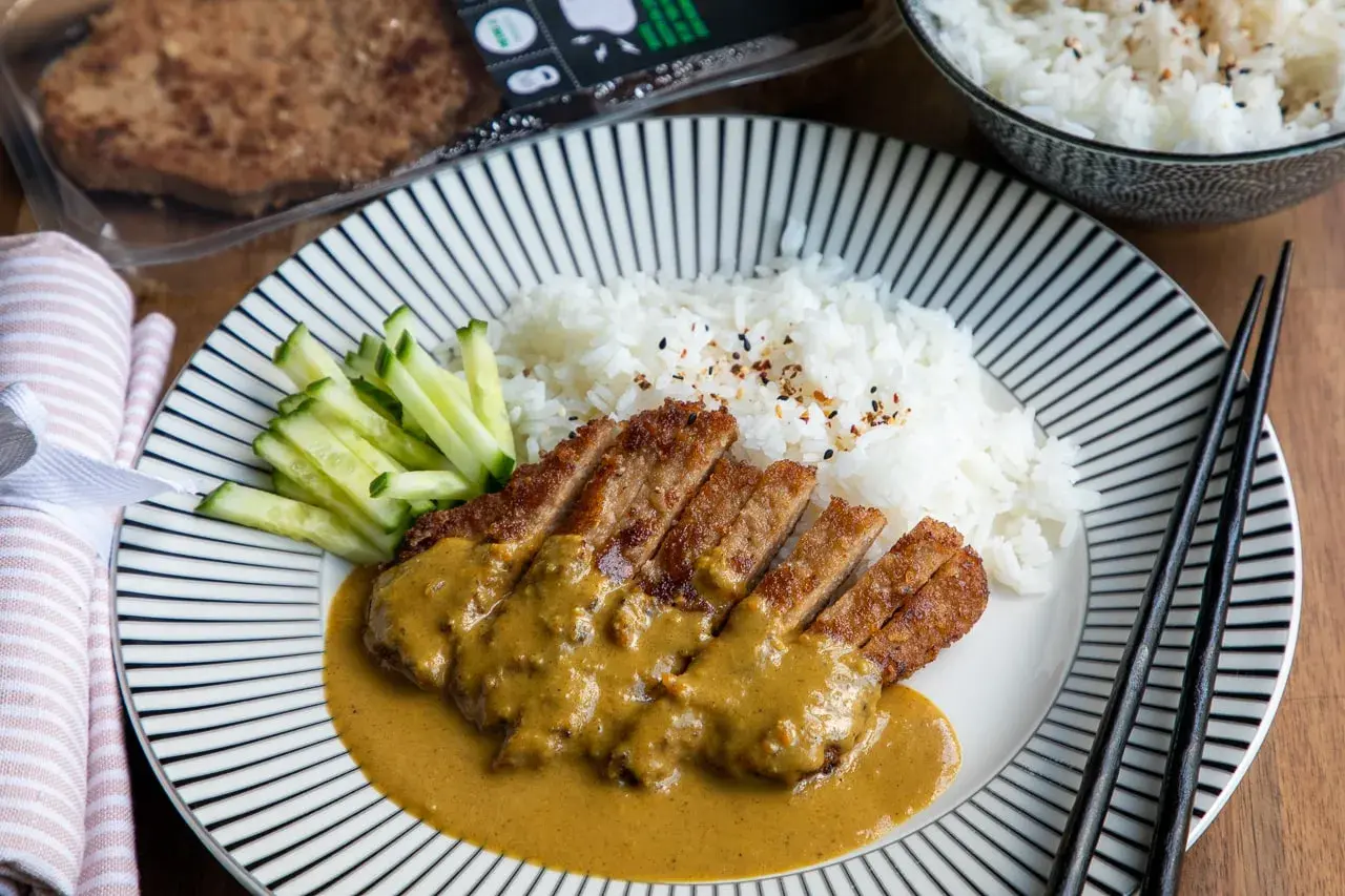 En tallrik med katsu curry, ris och gurka. Den panerade kotletten är skuren i skivor och täckt med en krämig currysås.