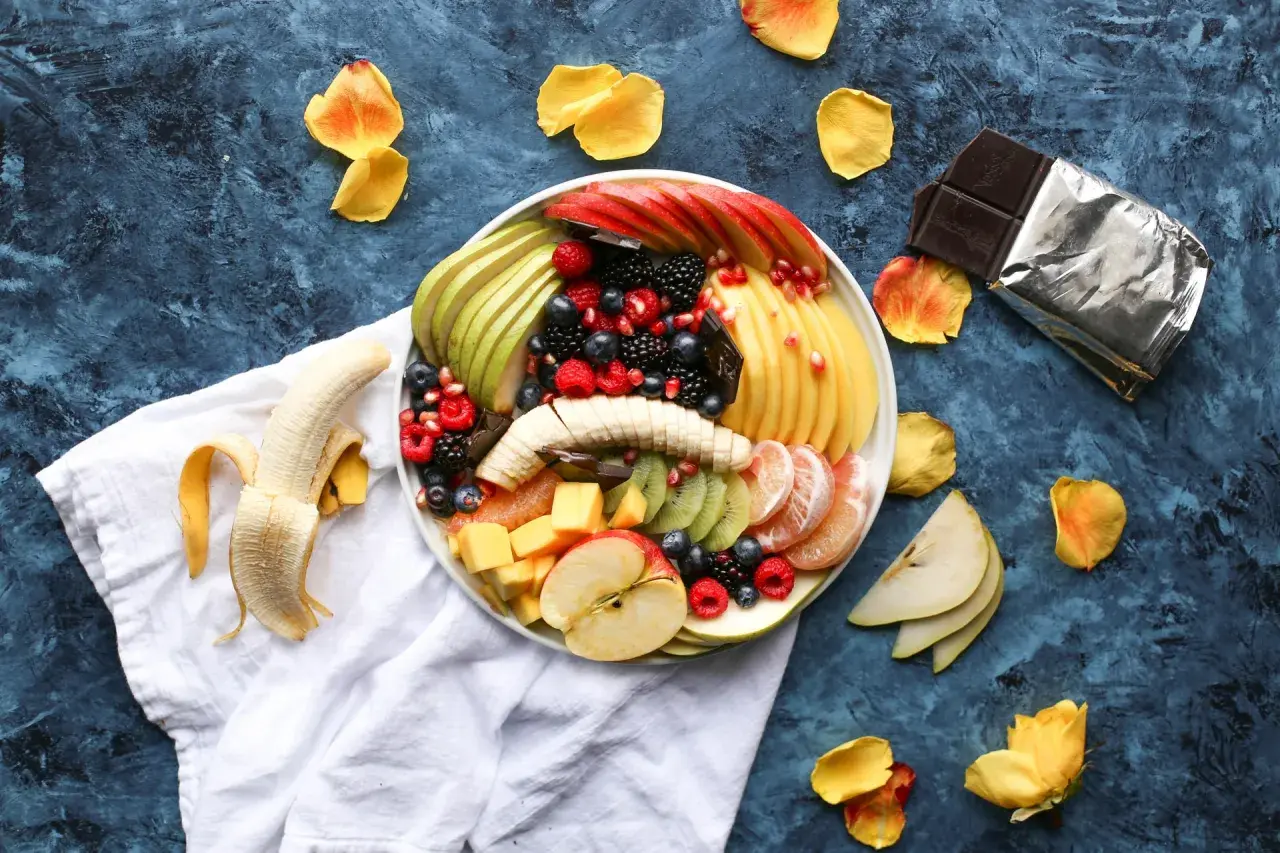 Plato de frutas variadas, incluyendo plátano, manzana, kiwi, bayas y cítricos. Es bueno comer fruta por la noche.