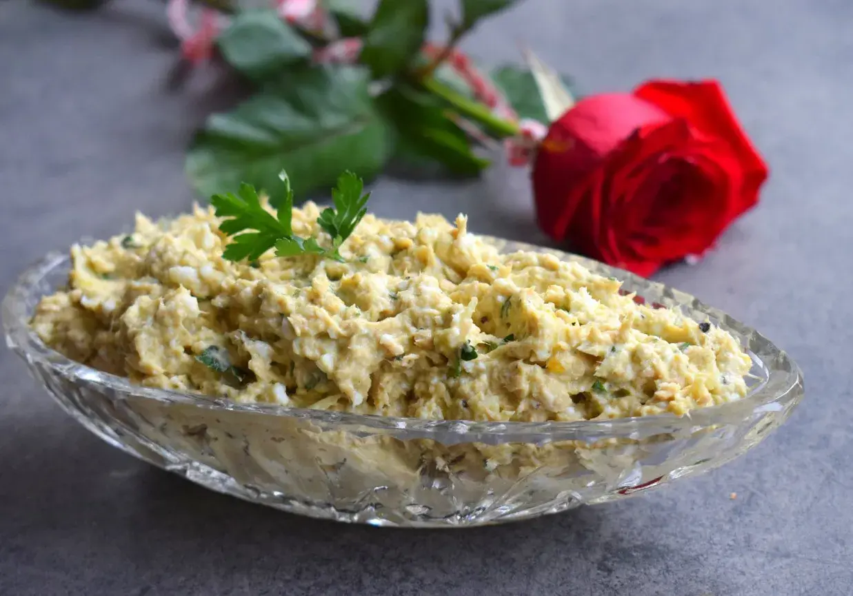 Pyszna pasta z awokado i tuńczyka, udekorowana natką pietruszki, w kryształowej misie. W tle czerwona róża.