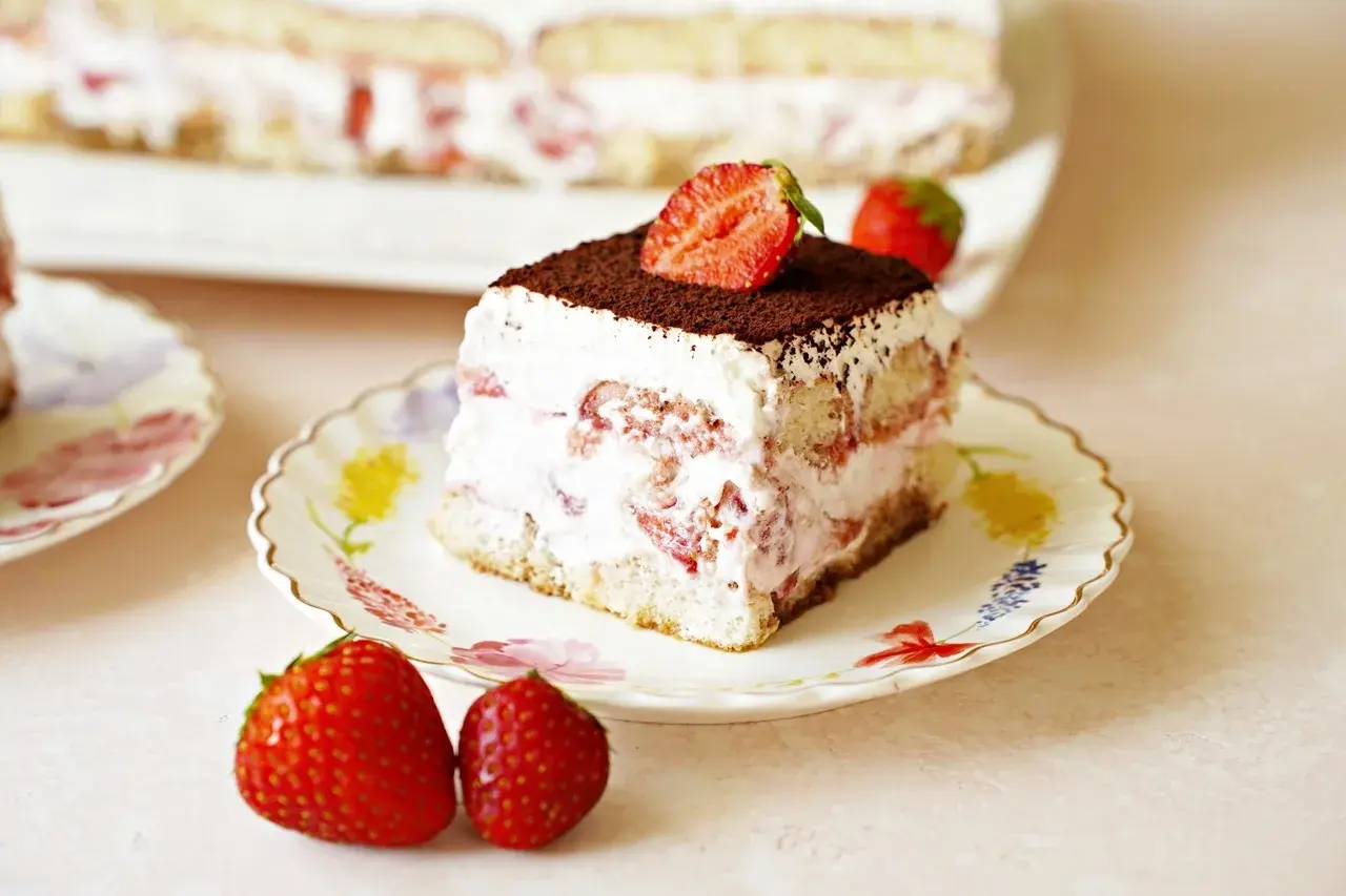Pyszne tiramisu truskawkowe z bitą śmietaną, biszkoptami i świeżymi truskawkami, posypane kakao.