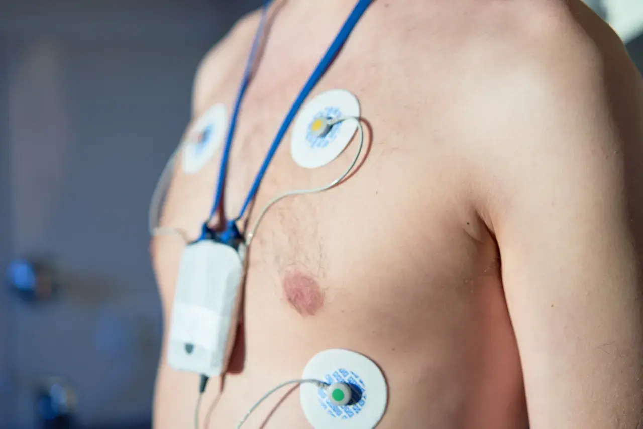 Mężczyzna z elektrodami EKG na klatce piersiowej, podłączony do urządzenia monitorującego. To właśnie holter, co to jest? Badanie serca.