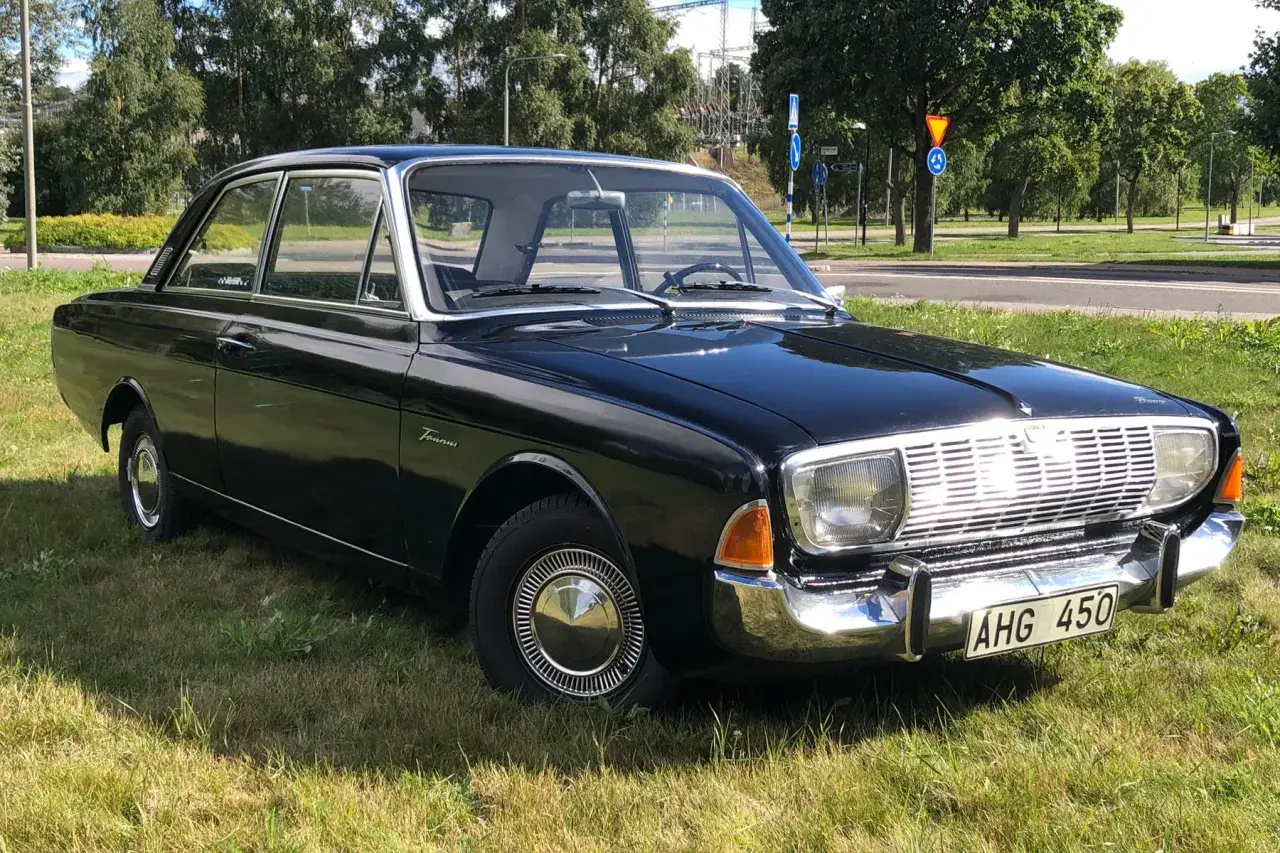 Svart Ford Taunus 1964, en klassisk bil med kromdetaljer, parkerad på en gräsmatta.