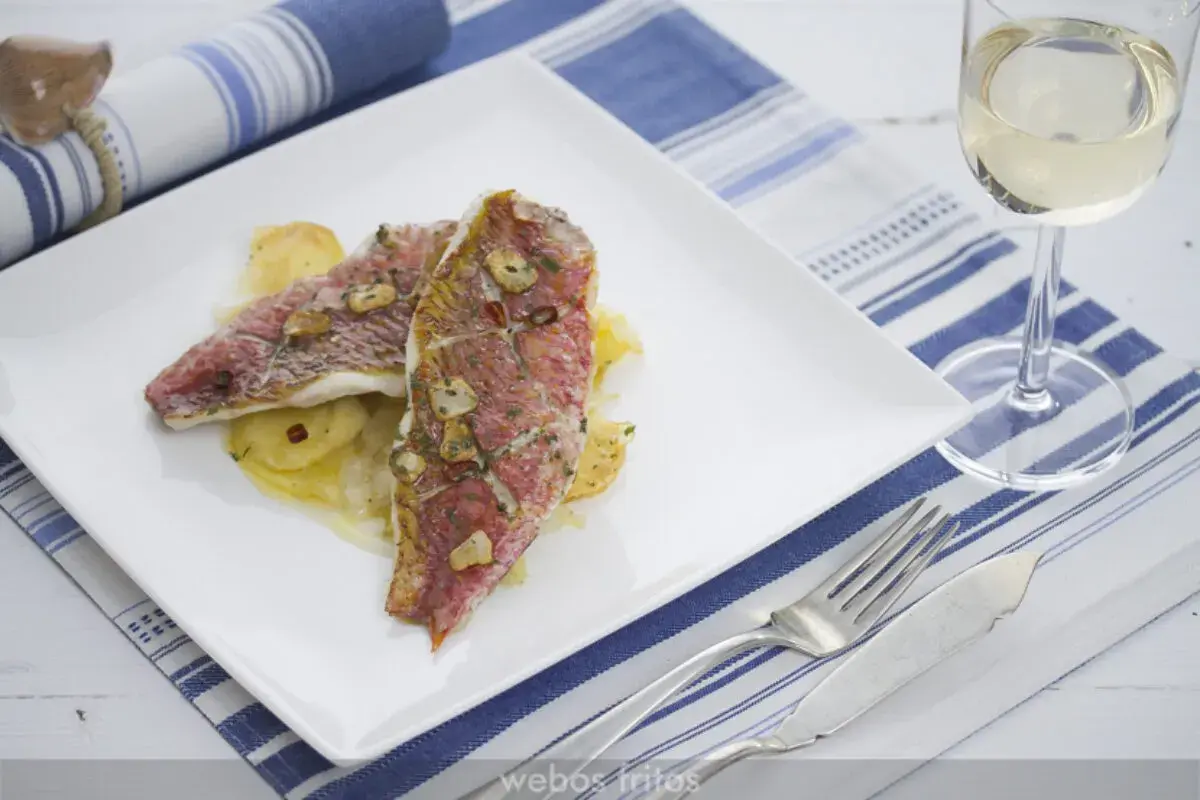 Dos deliciosos salmonetes al horno, con láminas de ajo y perejil, servidos sobre patatas. Un plato perfecto para disfrutar.