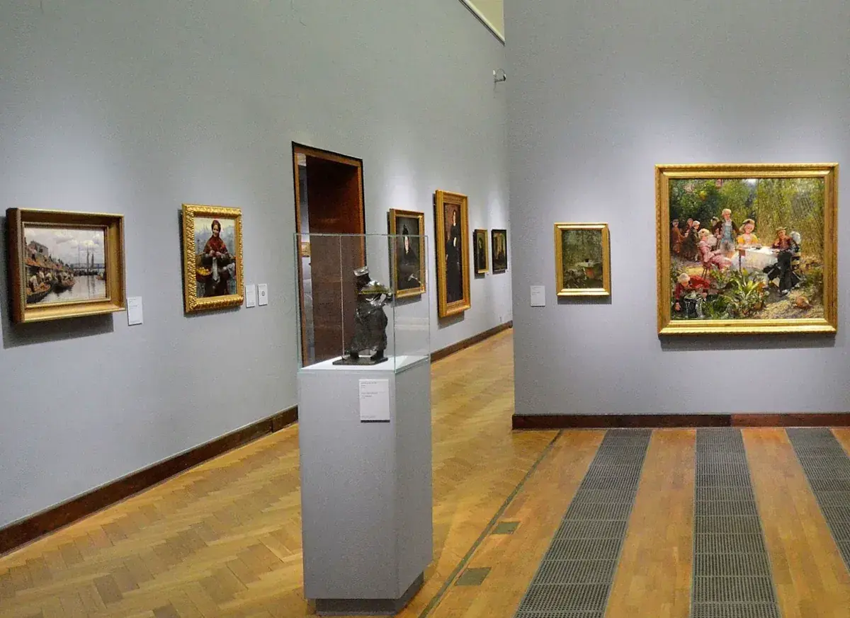 Obraz przedstawia galerię sztuki. Na ścianie wisi obraz z żydówką z pomarańczami.