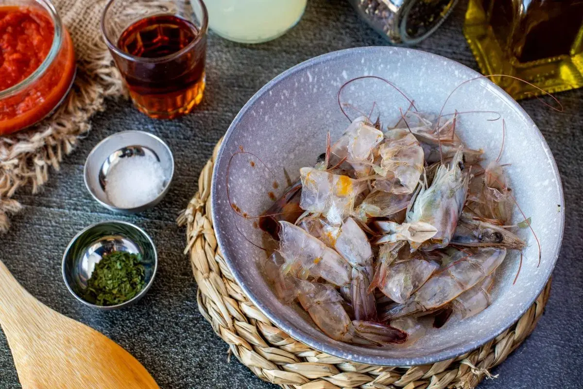 Cáscaras de camarón en un tazón, listas para hacer una sabrosa salsa americana. Ingredientes como tomate triturado, sal y hierbas acompañan.