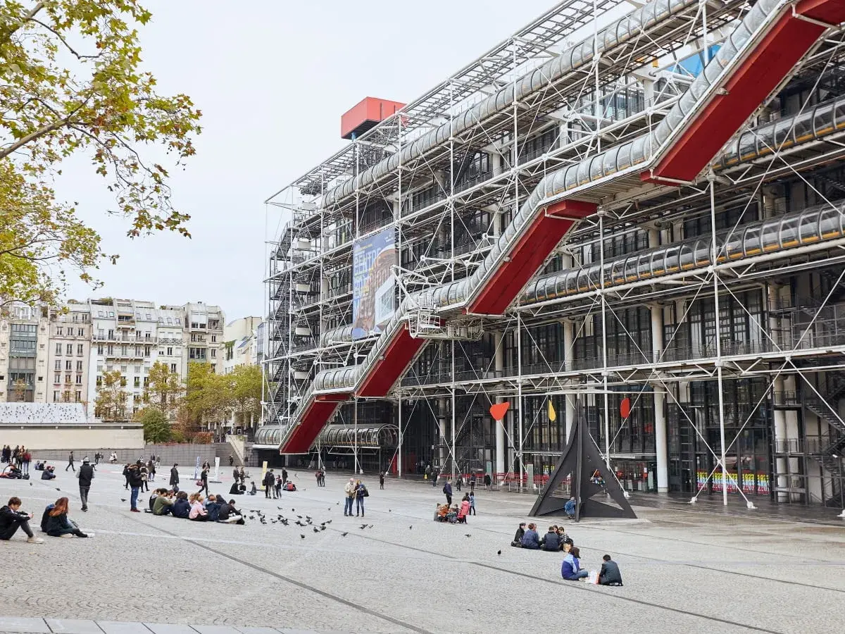 Centrum Pompidou w Paryżu z czerwonymi schodami ruchomymi i ludźmi na placu.