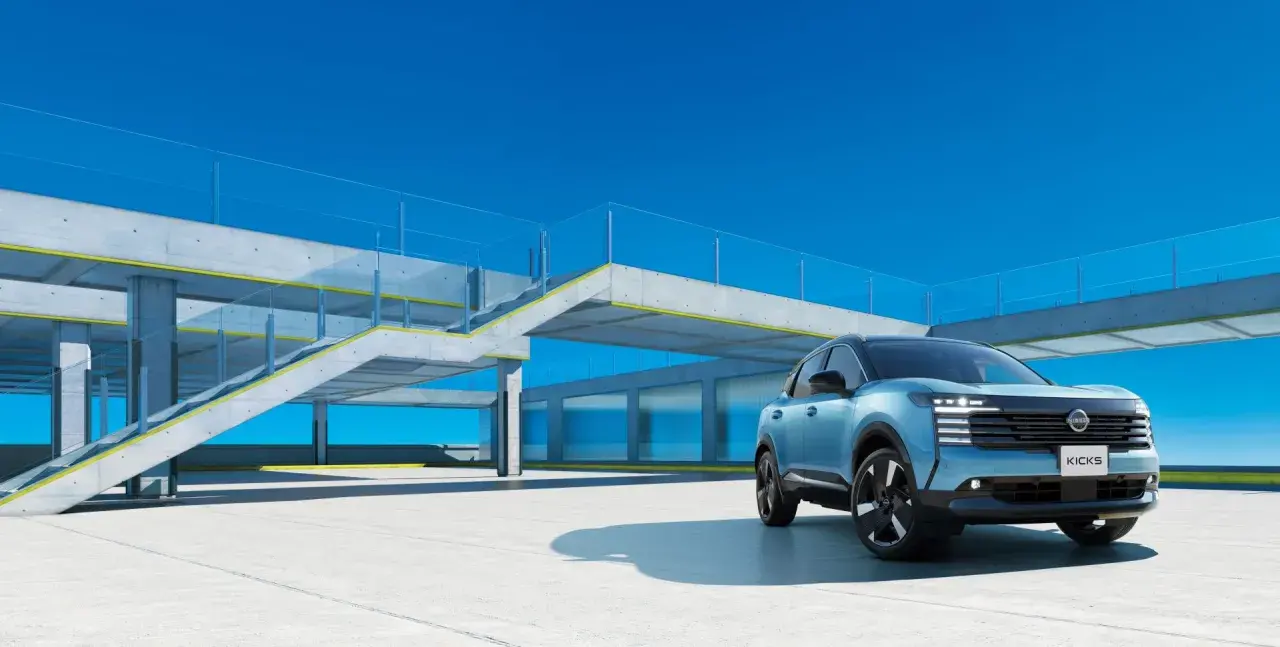 Niebieski Nissan Kicks stoi na betonowym placu przed nowoczesnym budynkiem z przeszklonymi oknami i betonowymi schodami.