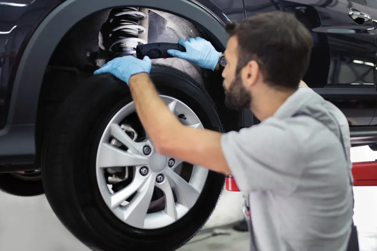Mecánico con guantes azules revisa el amortiguador de un coche. Es importante recordar que hay que cambiar los 4 amortiguadores a la vez para un rendimiento óptimo.