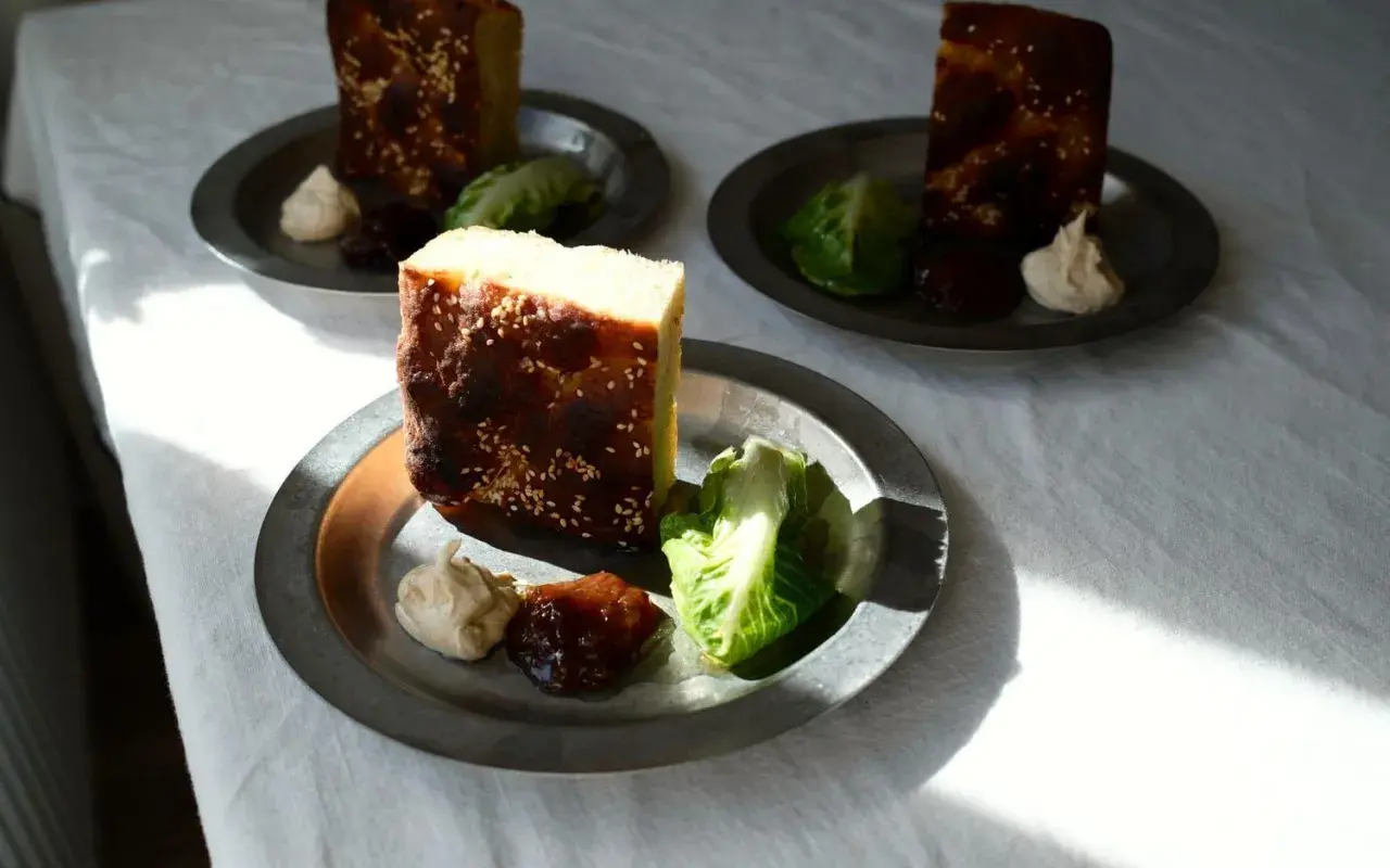 Enkel lyxig middag: bitar av rostat bröd med sesamfrön, serverade med sallad, en klick krämig röra och sylt på metalltallrikar.