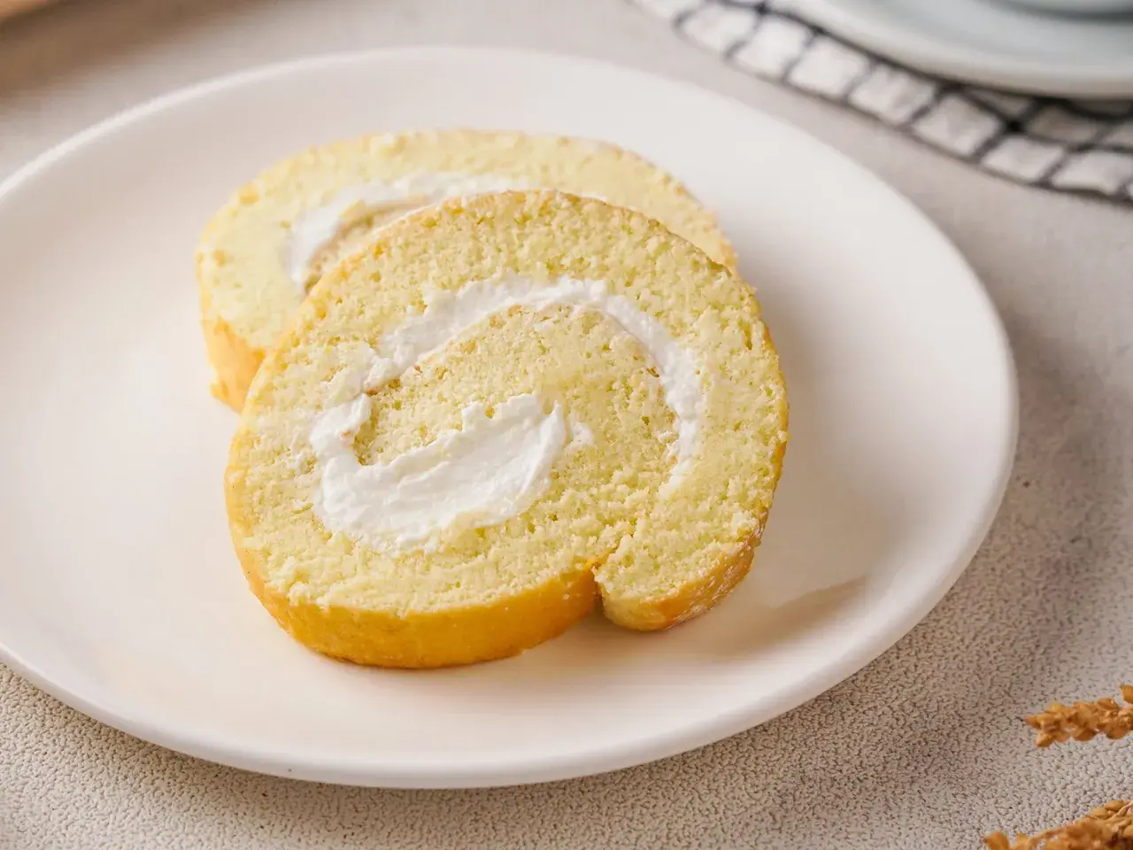Zwei Scheiben einer saftigen Zitronenrolle mit cremiger Füllung auf einem Teller. Ein einfaches Zitronenrolle Rezept zum Nachbacken.