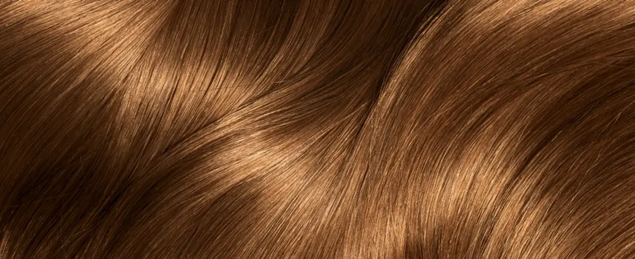 Capelli castani con riflessi dorati che ricordano i colpi di sole caramello, mossi e luminosi.