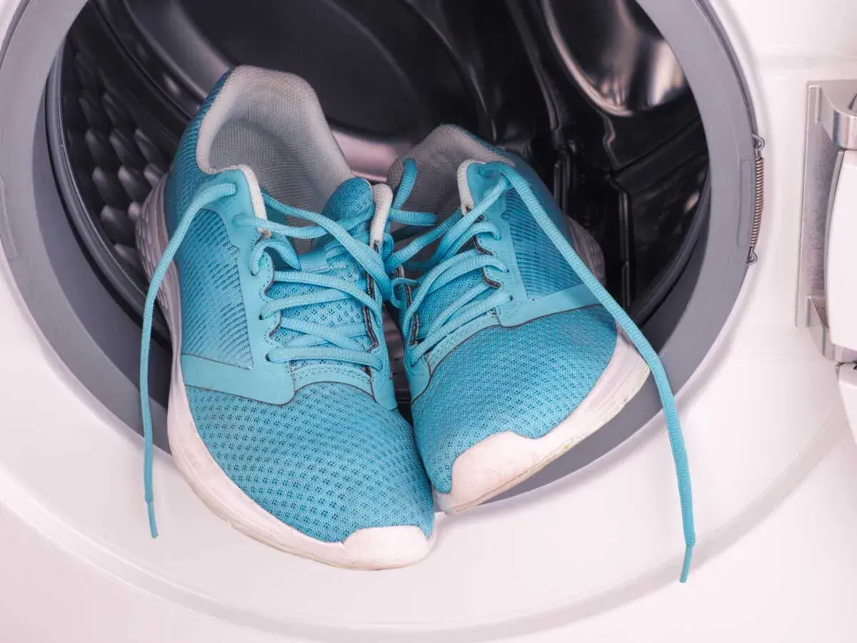 Paire de baskets bleues dans le tambour d'une machine à laver. Prêtes pour un cycle de nettoyage.