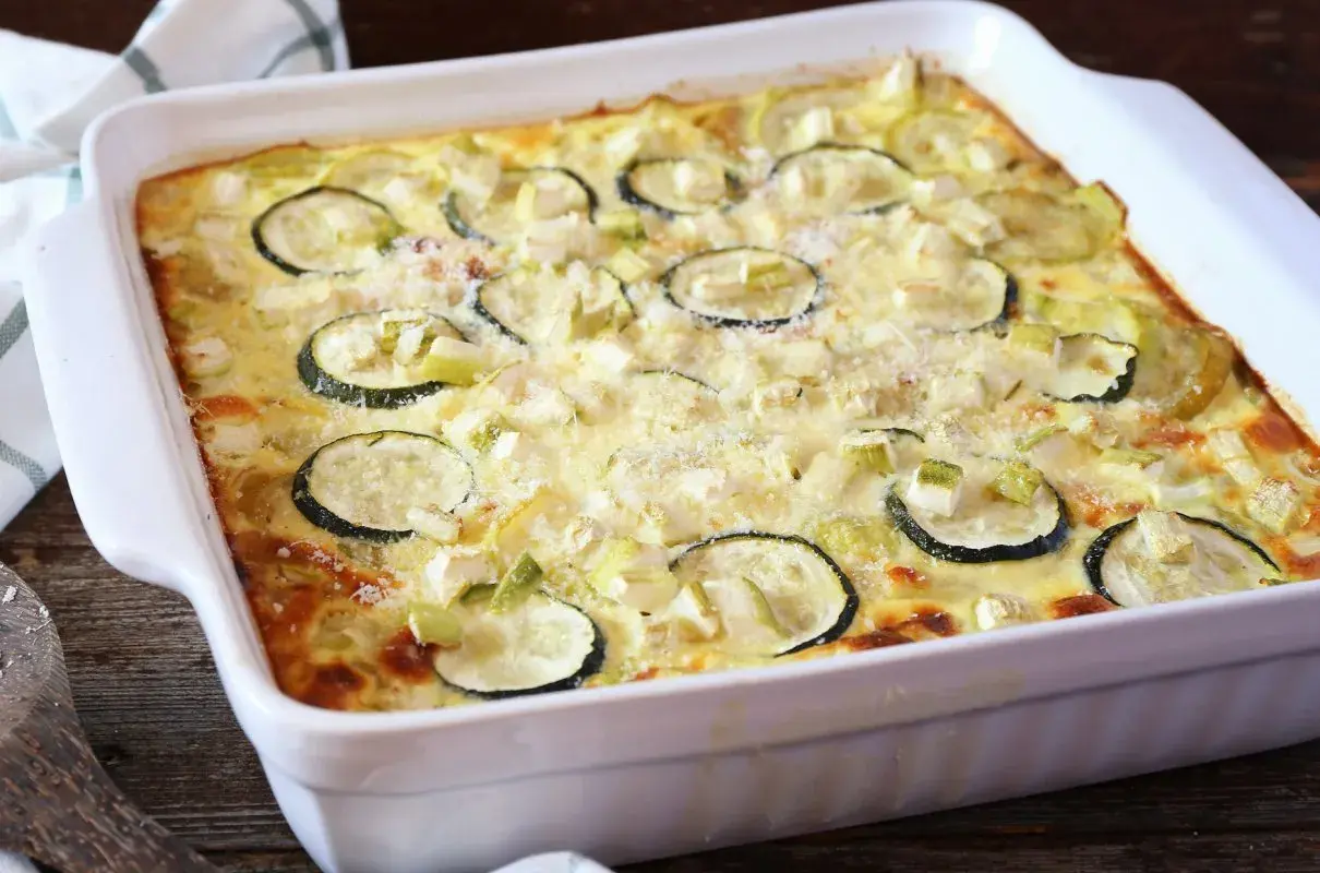 Pyszna zapiekanka z cukinii i mięsa mielonego, posypana parmezanem, w białym naczyniu żaroodpornym.