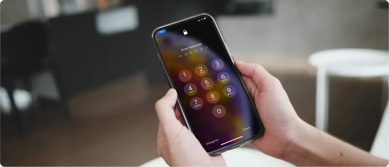 Dłonie trzymające iPhone'a z ekranem blokady i klawiaturą numeryczną.