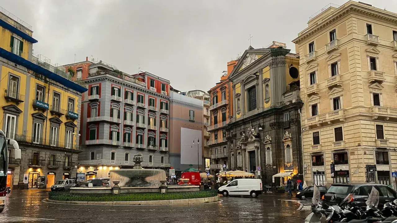 Rainy day in Naples, with colorful buildings, a fountain, and parked scooters. A perfect scene for a 2 days in Naples adventure.