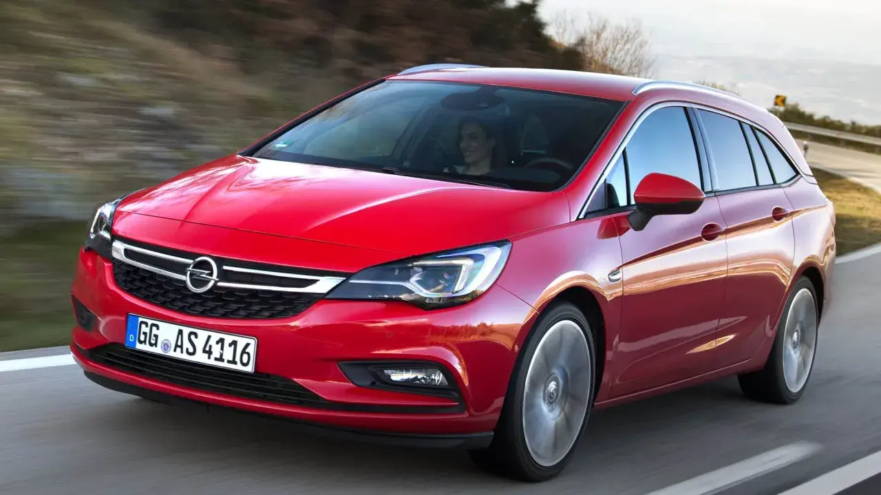 Röd Opel Astra kombi 2016 körs på en väg. En kvinna syns bakom ratten. Kanske ett problem med bilen?