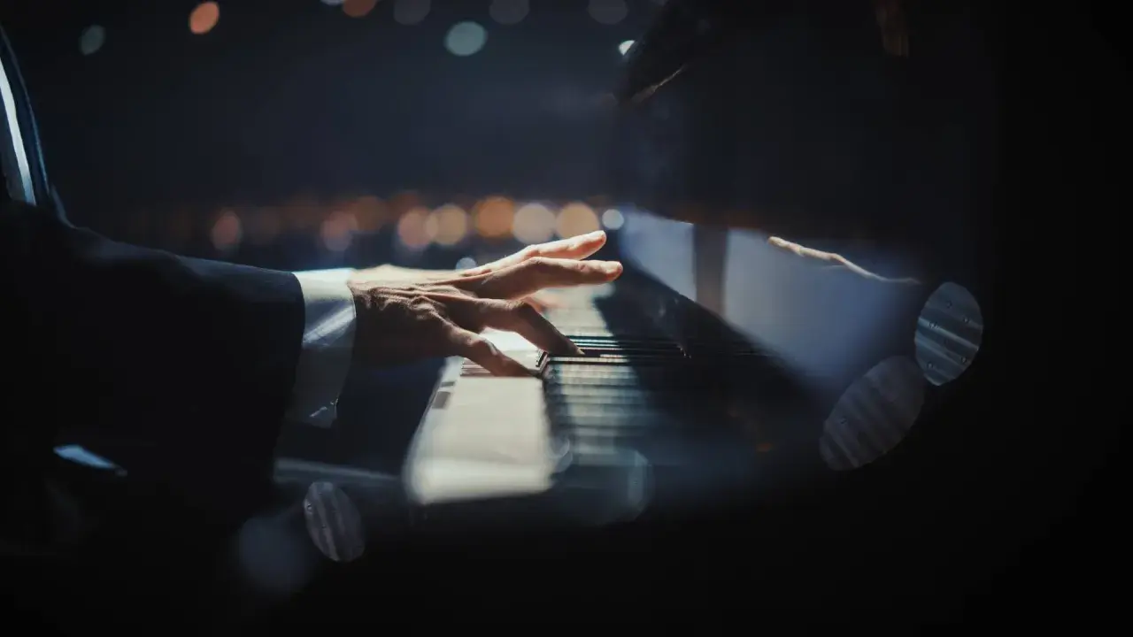 Dłoń pianisty grająca nokturn na fortepianie, w tle rozmyte światła.