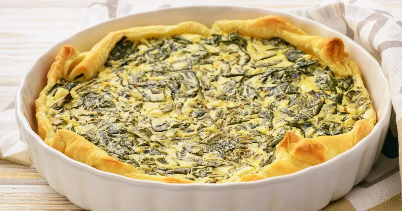 Pyszny quiche ze szpinakiem w białej formie, idealny pomysł na to, jak jeść szpinak. Złociste ciasto i kremowe nadzienie.