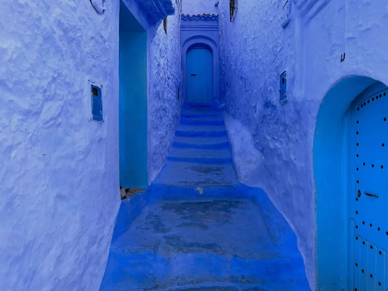 Callejón azul en Chefchaouen, con escalones que suben hacia una puerta. A pesar de su belleza, Chefchaouen es peligroso para los que se pierden en sus laberintos.