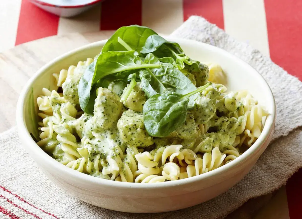 Pyszny makaron z kurczakiem w kremowym sosie pesto, udekorowany świeżym szpinakiem. Idealny obiad dla całej rodziny.
