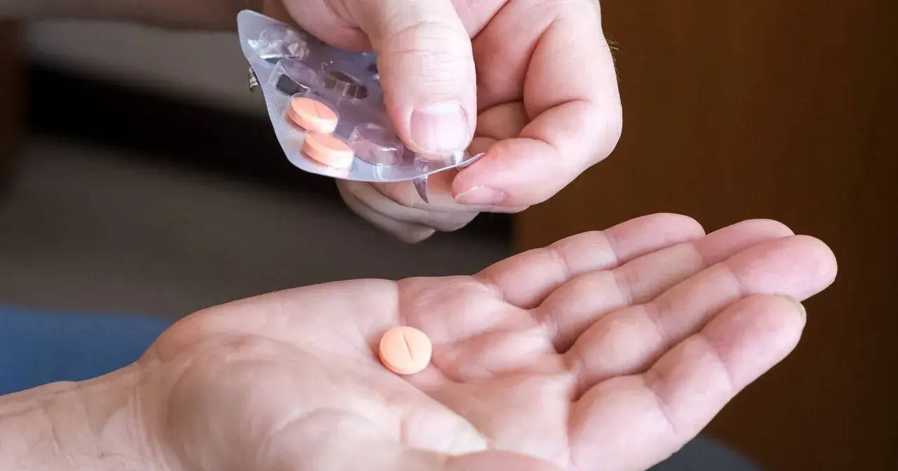 Dłoń przyjmuje pomarańczową tabletkę na cholesterol z blistra.