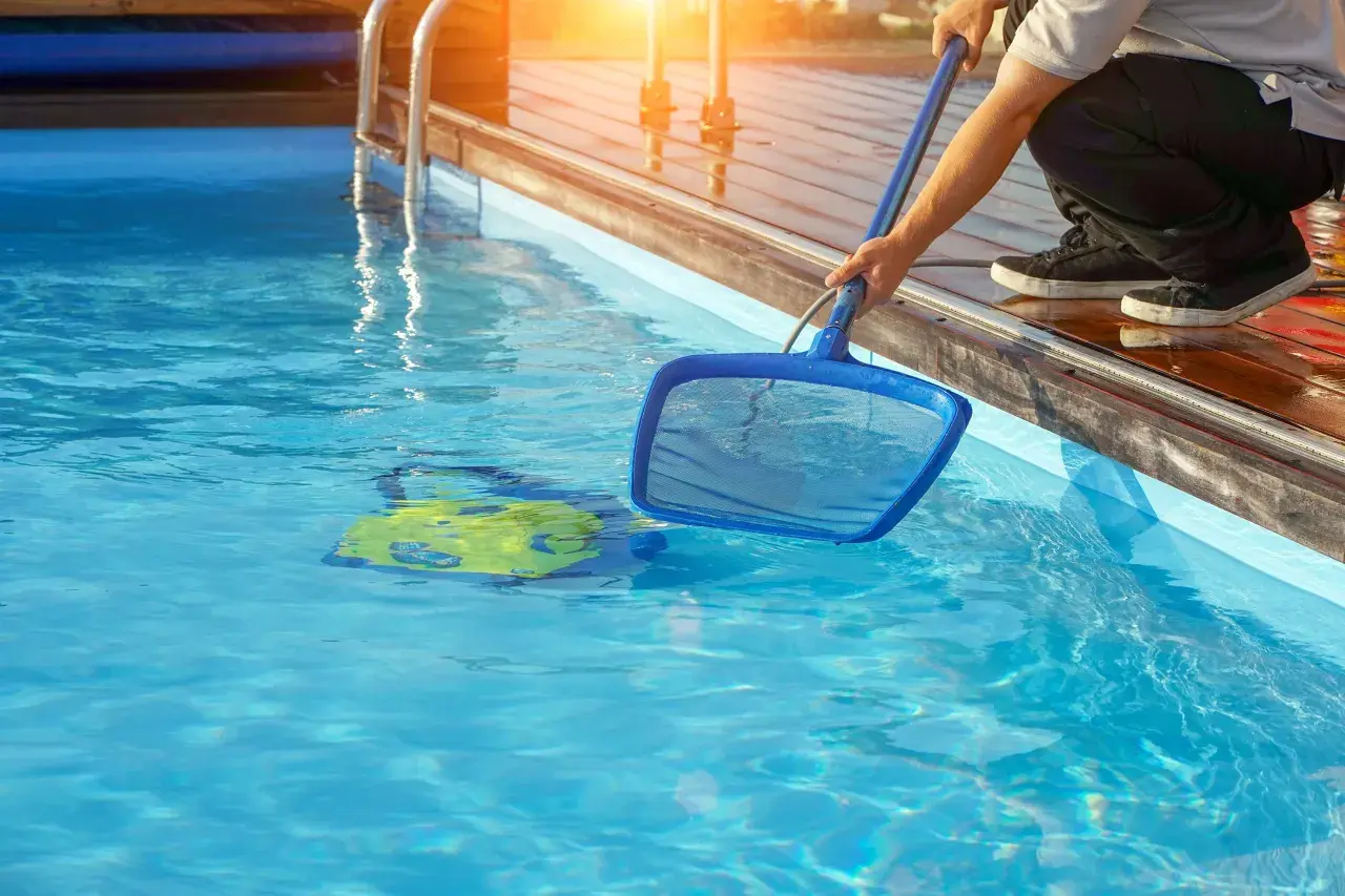 Mann reinigt den Pool mit einem Kescher. Ein gelbes Spielzeug schwimmt im klaren Wasser.