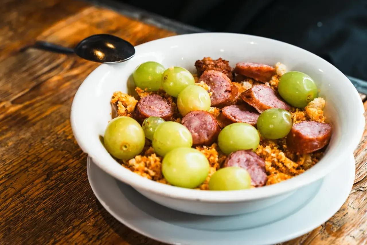 Un plato con uvas verdes, chorizo en rodajas y migas crujientes, un sabor que recuerda a el tubo zaragoza.