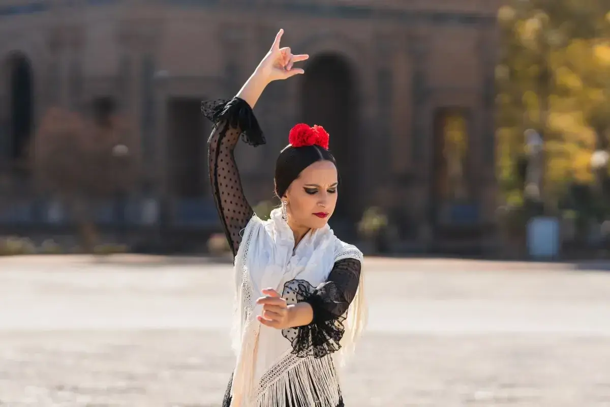Bailarina de flamenco con un vestido blanco y negro, flor roja en el pelo, moviendo sus brazos al ritmo rumba.